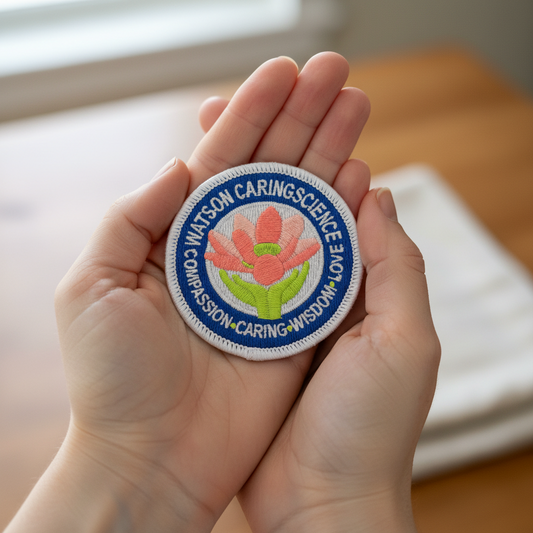 Hand holding a patch with 'Watson Caring Science' logo design featuring a lotus flower and the text 'Compassion, Caring, Wisdom, & Love'.